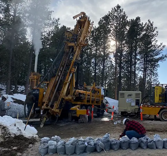 RC drill rig operating on a snow-covered pad in South Dakota with crew member managing sample bags