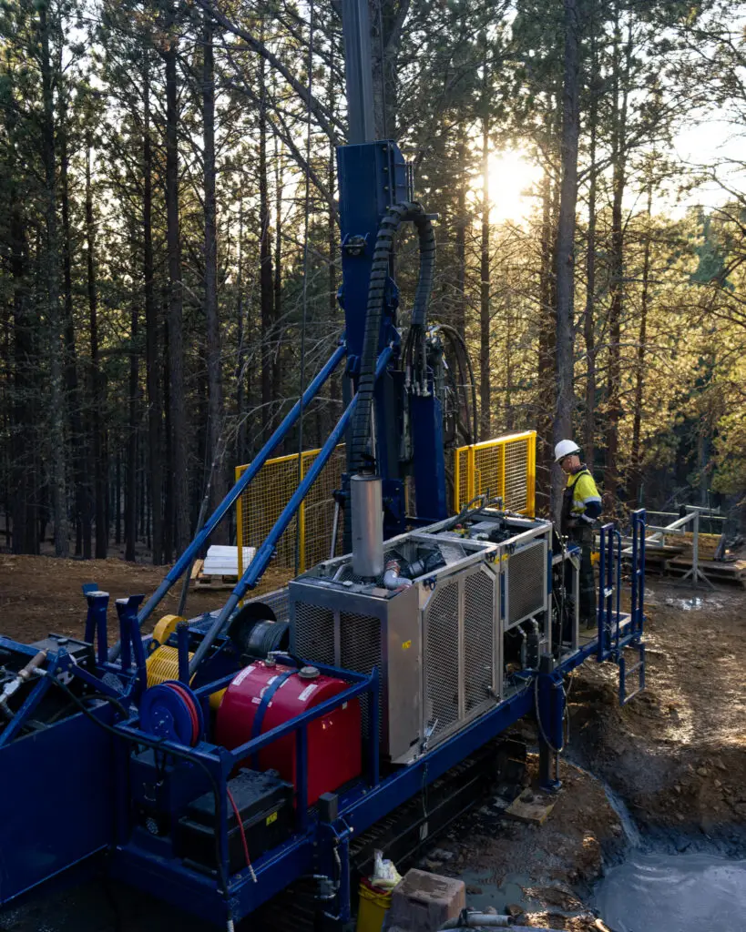 Core drilling rig operating in dense forest at sunrise with worker on rig platform